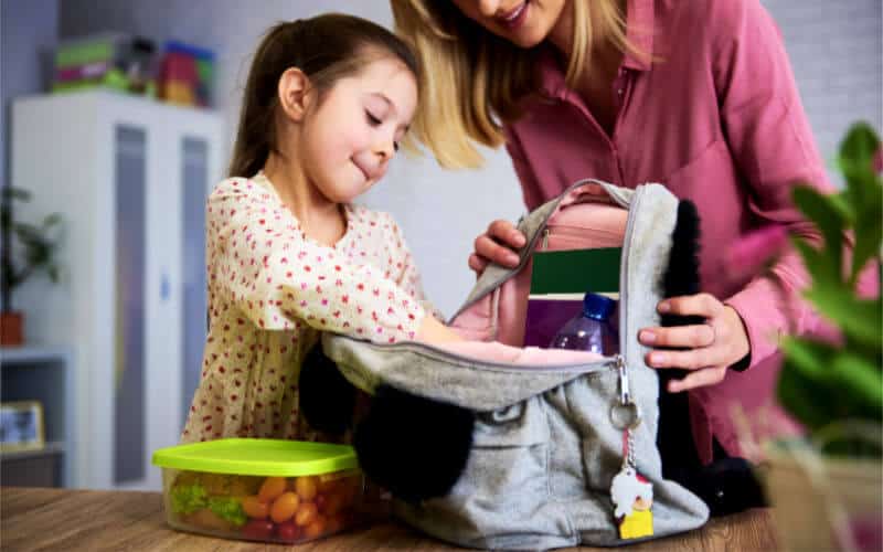 Small child helping her mom pack her bookbag for school.
