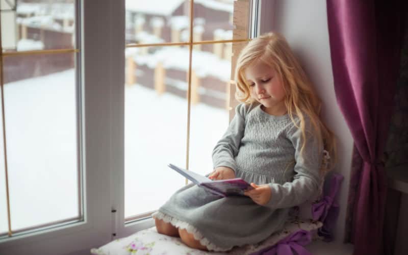 Child sitting in a window reading a book about starting school.
